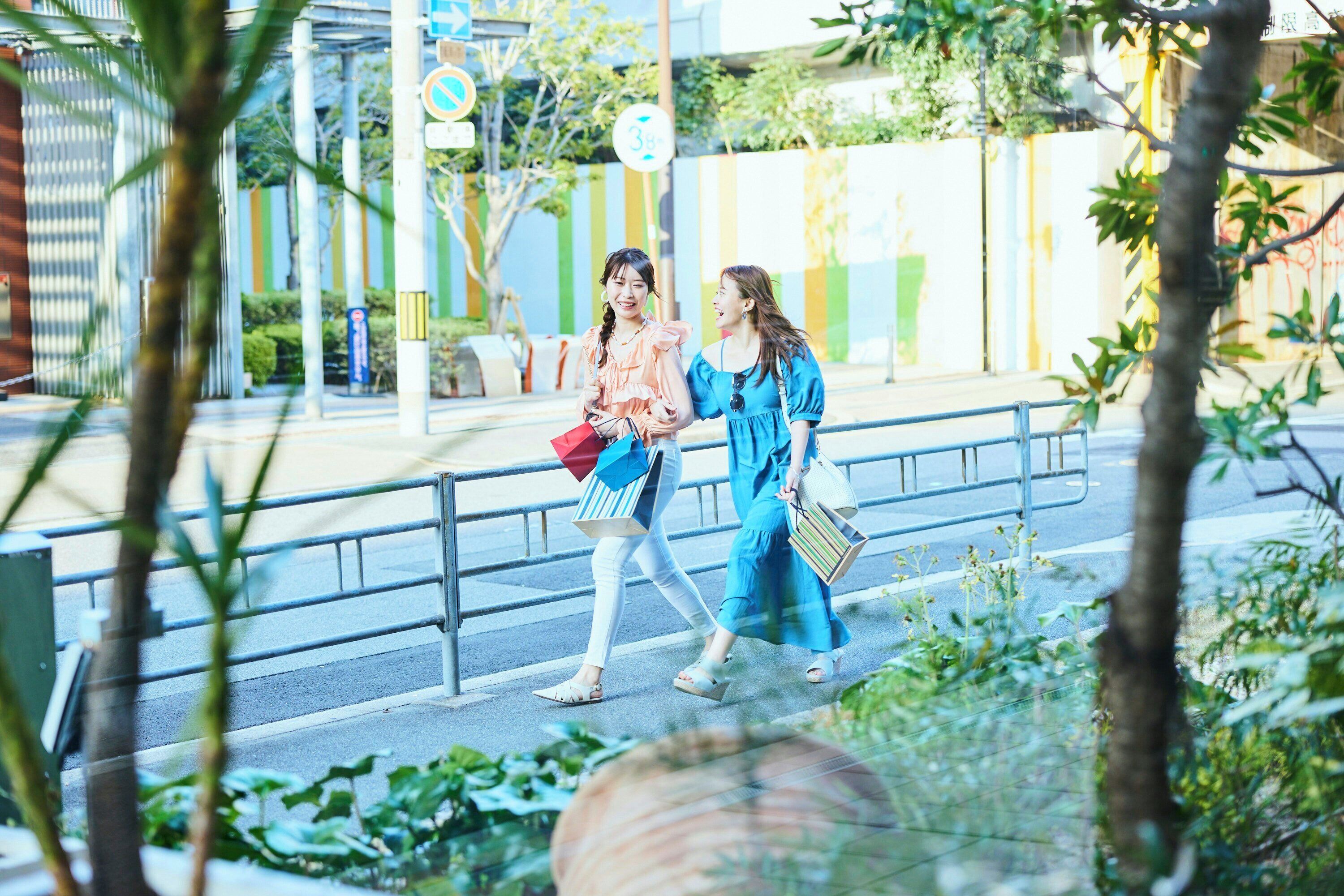 Two people walking on a sidewalk with a metal railing and greenery in the foreground.