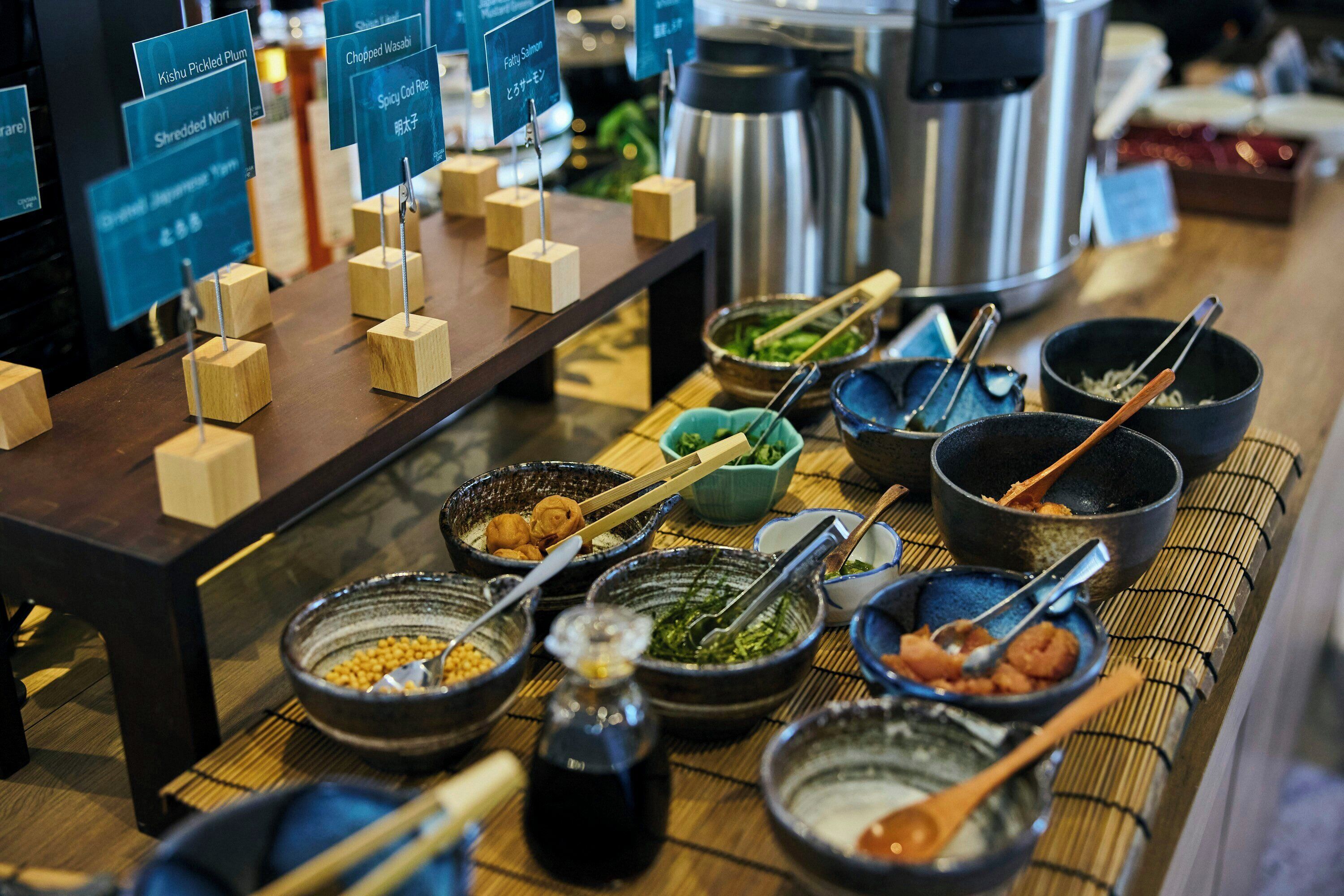 A buffet table with various dishes and condiments, including bowls of food, chopsticks, and condiment containers.
