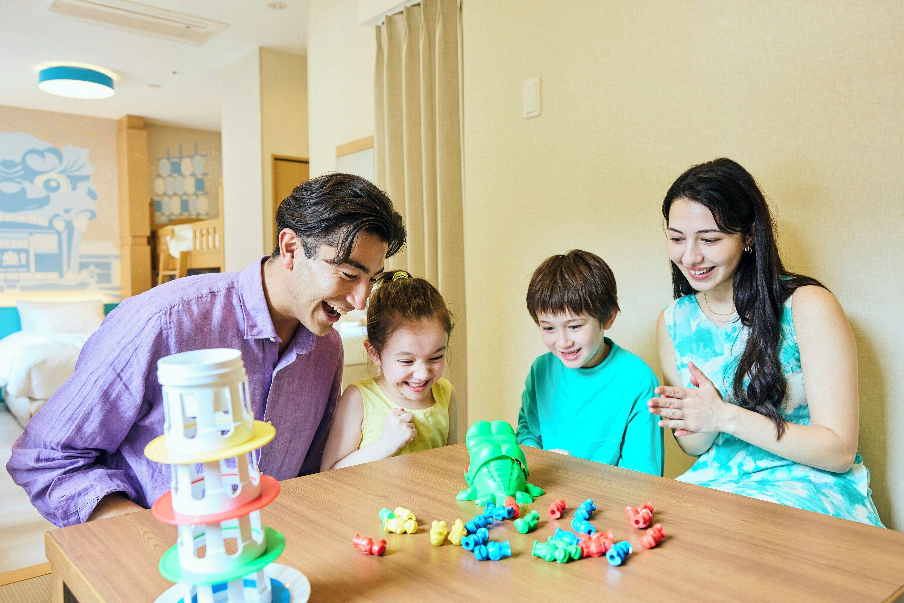 A family playing with toys at a wooden table in a room with a simple, neutral decor.