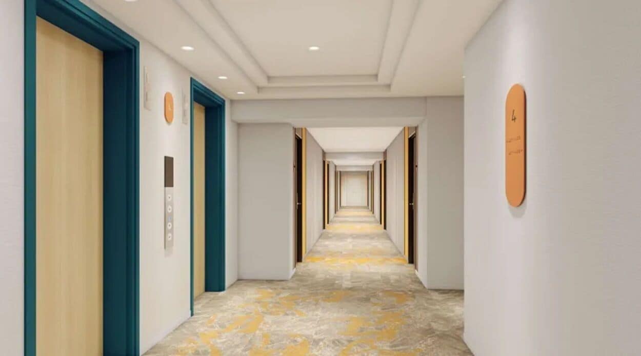 A long, narrow hallway with doors on both sides, a clock on the left wall, and a number sign on the right wall.