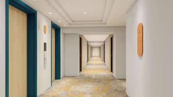 A long, narrow hallway with doors on both sides, a clock on the left wall, and a number sign on the right wall.