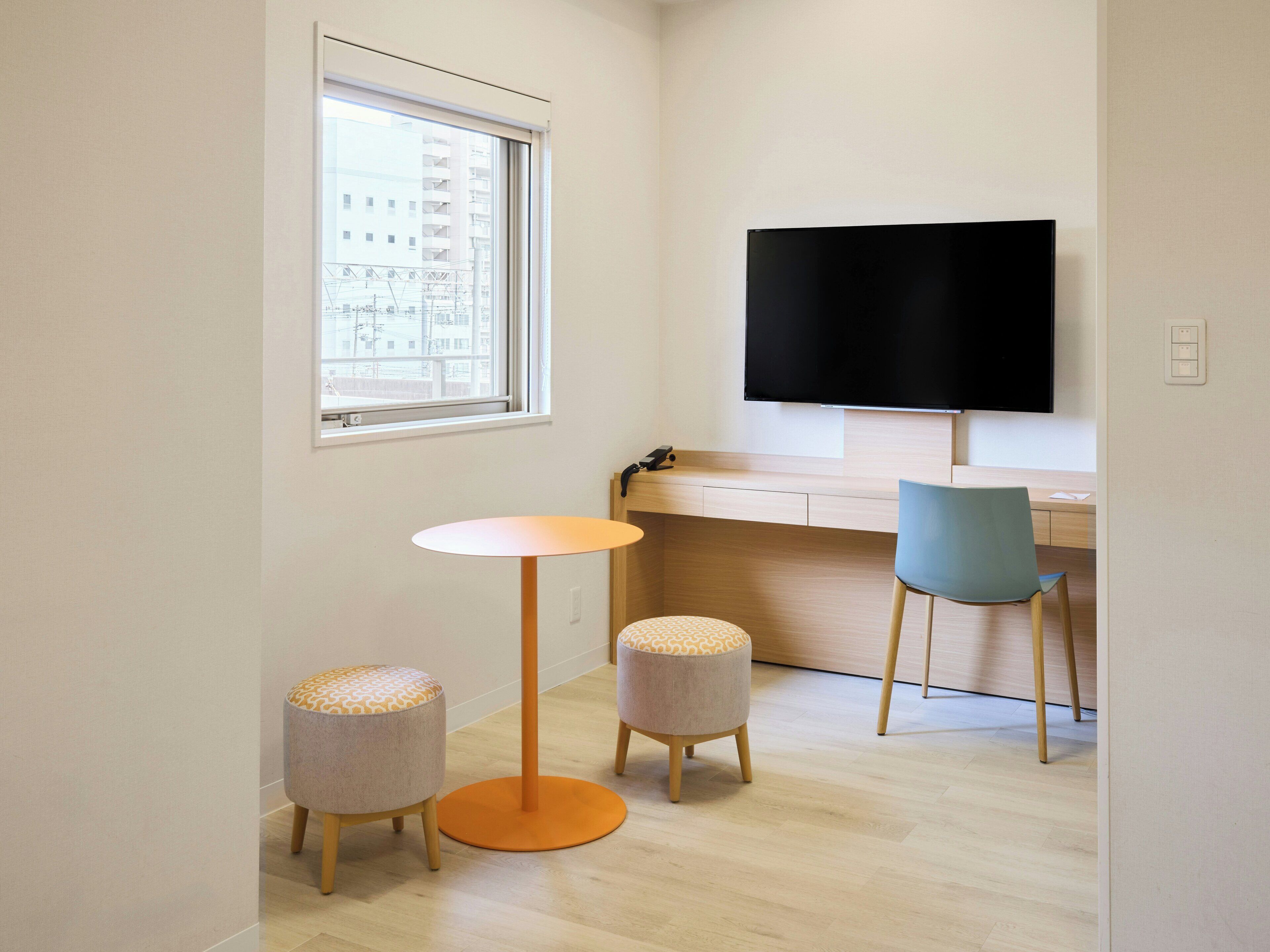 A small room with a desk, a chair, a round table, and a TV mounted on the wall.
