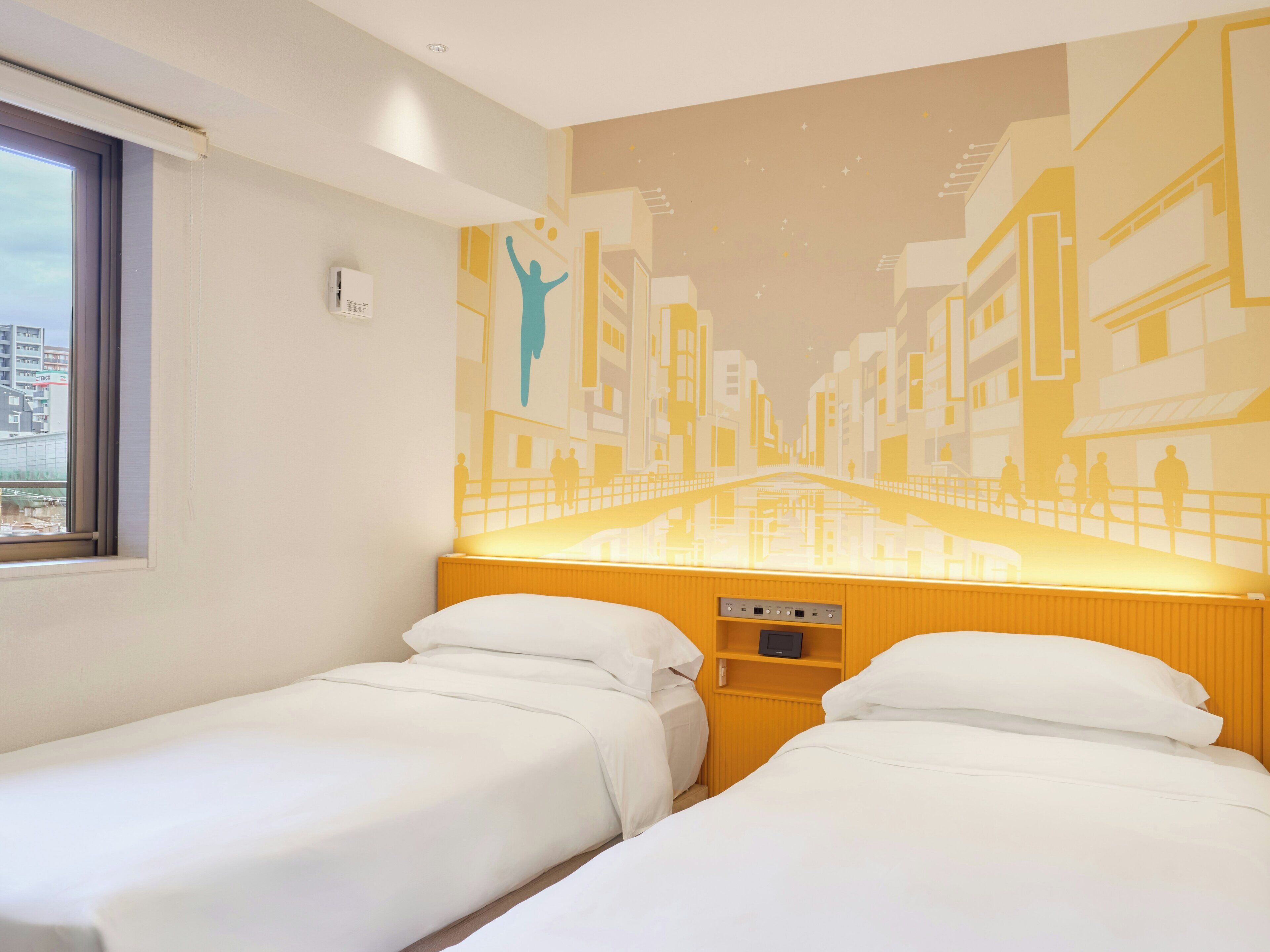 A hotel room with two beds, a window, a wall mural, and a control panel.