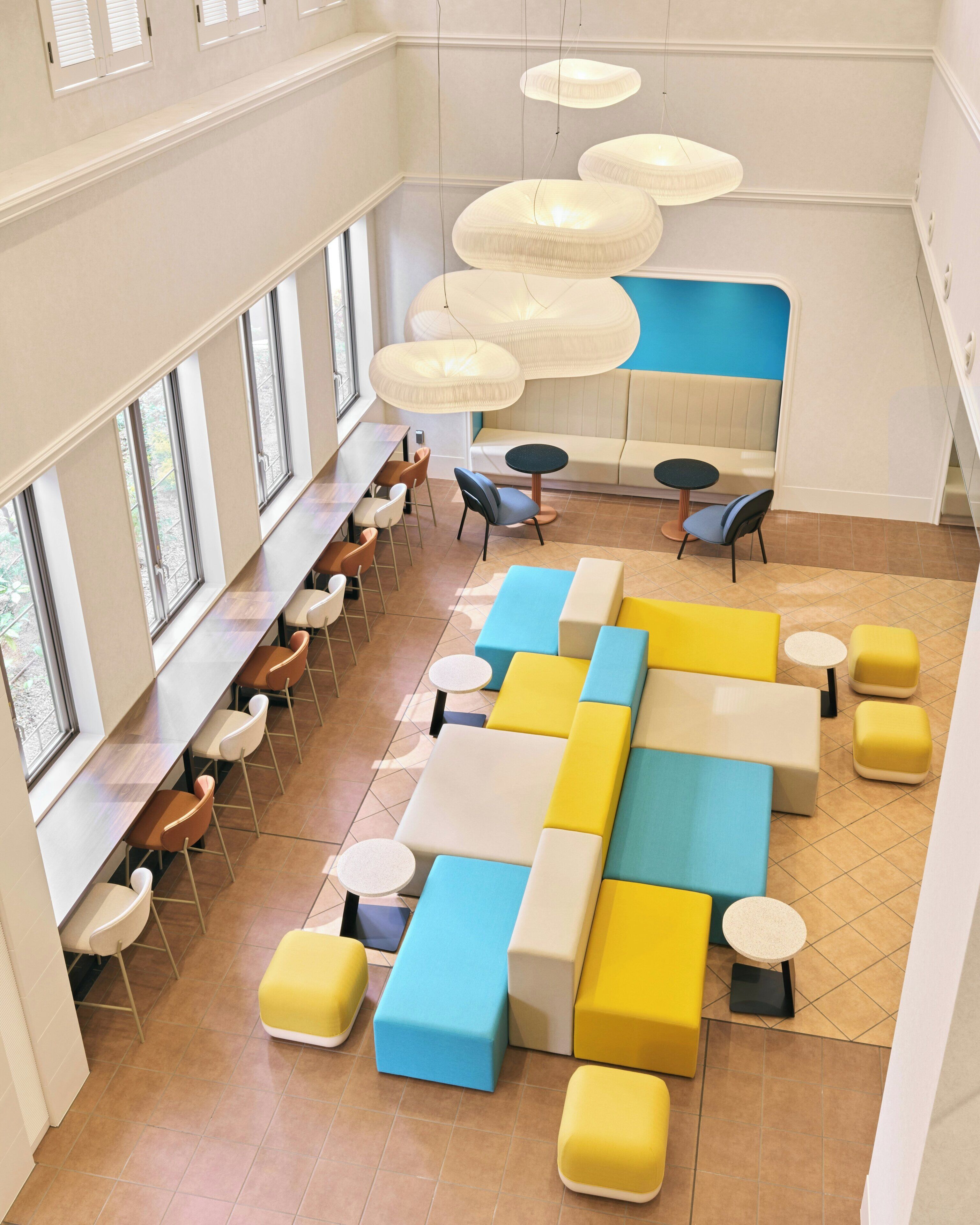 A modern interior with a long dining area, multiple seating options, and a large window providing natural light.
