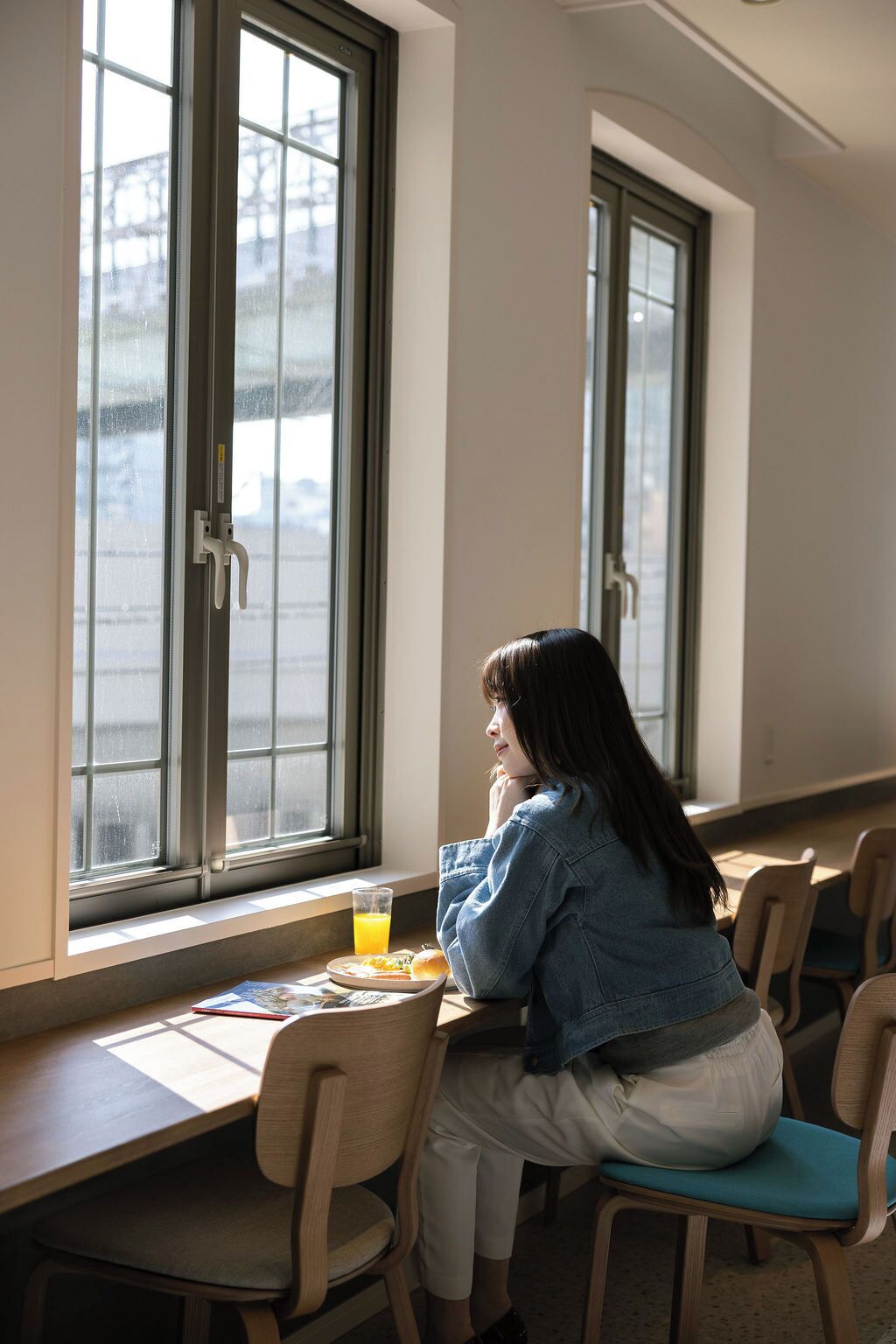 Une personne est assise à une table près d’une fenêtre, d’où l’on peut voir un bâtiment à l’extérieur.