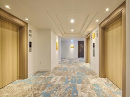 A hotel hallway with wooden doors, a patterned carpet, and ceiling lights.