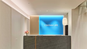 Ein Empfangstresen mit einem blauen Bildschirm, der 'CENTARA LIFE' anzeigt, und einer Vase mit Blumen.