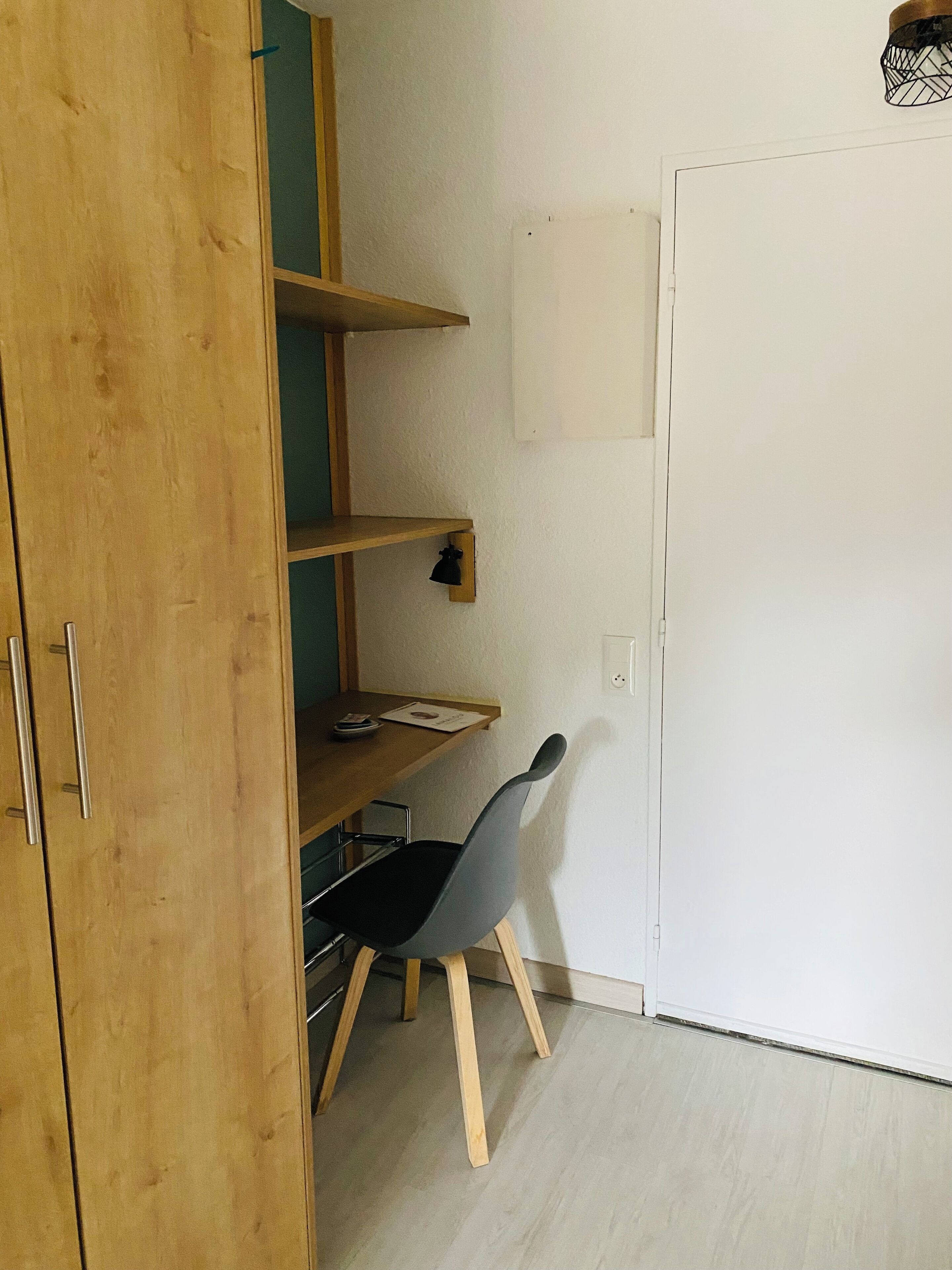Une pièce avec une armoire en bois, un bureau avec une chaise et un mur blanc avec un interrupteur.