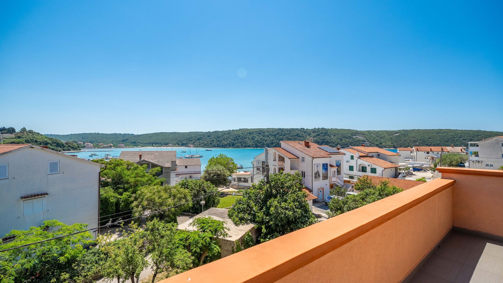 A coastal residential area with buildings, trees, and a clear view of the sea.