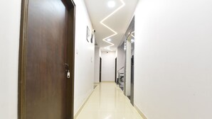 A hallway with a wooden door, a tiled floor, and a modern ceiling design. - Ricch Hotels (Jaipur)
