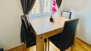 Ein kleiner Essbereich mit Tisch und Stühlen, ein Fenster mit Vorhängen und Blick auf Gebäude.
