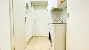 Ein schmaler Flur mit einer Waschmaschine und einem Waschbecken an einer Seite sowie einer Tür am Ende.