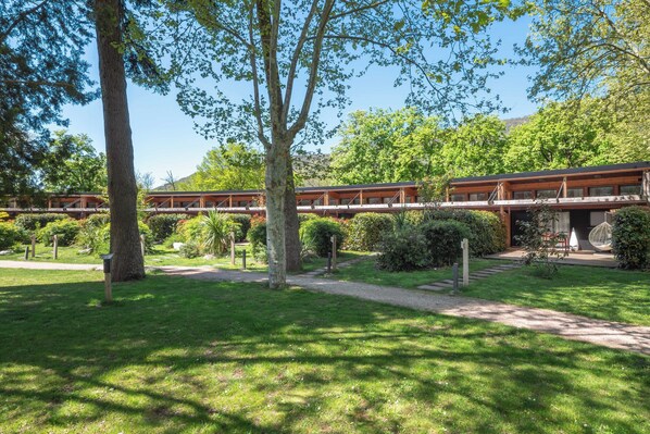 Un bâtiment en bois doté d’une allée couverte, entouré d’une végétation luxuriante et d’arbres.
