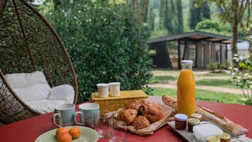 Taula amb menjar i begudes, una cadira de vimetla i vista a un jardí.