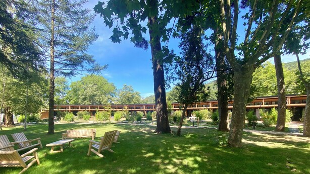 Een rustige buitenruimte met houten stoelen en tafels, omgeven door weelderige begroeiing en bomen.