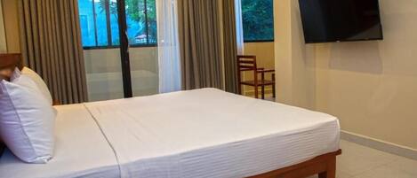 A hotel room with a bed, a TV mounted on the wall, a chair, and a window with curtains.