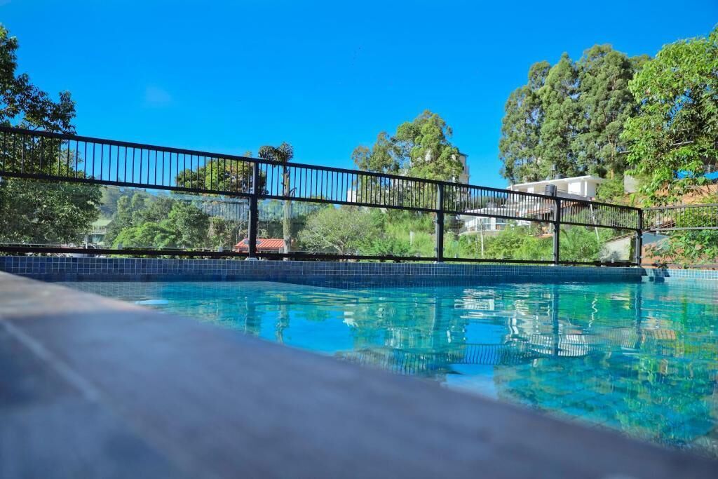 A clear blue swimming pool with a metal railing, surrounded by lush greenery and trees.