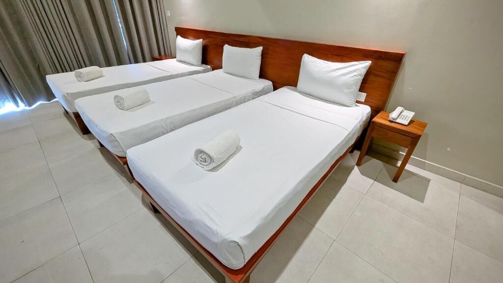 A hotel room with three single beds, each with a wooden headboard and white linens. There is a wooden nightstand with a telephone on it.
