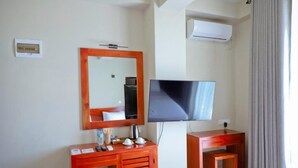 A hotel room with a wooden desk, a television, a mirror, and an air conditioning unit. - Oak Ray La Ella Breeze (Ella)