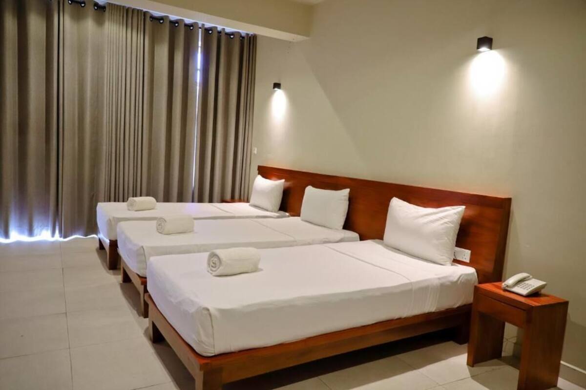 Een hotelkamer met twee bedden, een houten hoofdbord, een nachtkastje met een telefoon en een gordijn.
