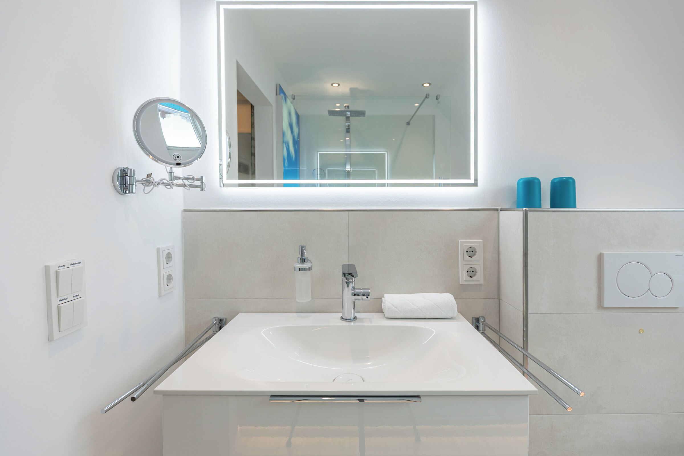Une salle de bain moderne avec un grand miroir, un lavabo blanc et une douche à parois de verre.