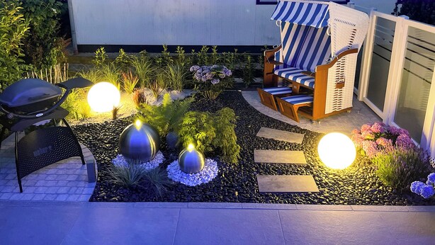 A well-lit outdoor seating area with a striped lounge chair, a grill, and decorative lighting. - Vacation home "Bellaeins" in Tönning for up to 4 people (Tönning)