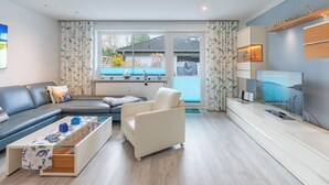 A modern living room with a sofa, a white armchair, a coffee table, and a TV on a wooden stand. - Vacation home "Bellaeins" in Tönning for up to 4 people (Tönning)