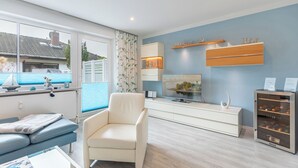 A modern living room with a sofa, a chair, a TV, a cabinet, and a small refrigerator. - Vacation home "Bellaeins" in Tönning for up to 4 people (Tönning)