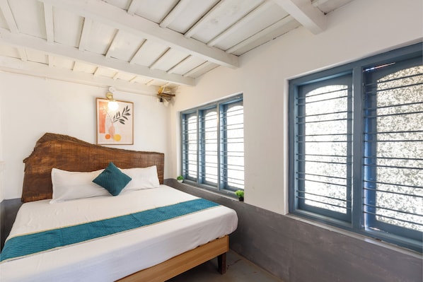A bedroom with a wooden bed, white bedding, a teal throw, and a window with blue shutters. - Underground Hostel By Bilwa Estate (Madikeri)