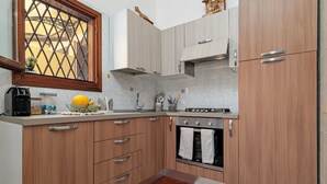 A kitchen with wooden cabinets, a built-in oven, and a window with a decorative grille. - Holiday Home 'Villetta Via Tempio' with Private Terrace, Private Garden and Air Conditioning (San Teodoro)