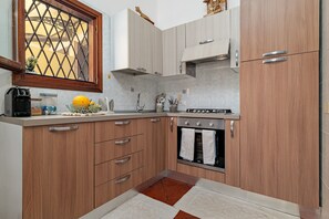 A kitchen with wooden cabinets, a built-in oven, and a window with a decorative grille. - Holiday Home 'Villetta Via Tempio' with Private Terrace, Private Garden and Air Conditioning (San Teodoro)