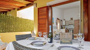 A dining table set with plates, glasses, and a bottle of wine, with a wicker chair and a wooden door in the background. - Holiday Home 'Villetta Via Tempio' with Private Terrace, Private Garden and Air Conditioning (San Teodoro)