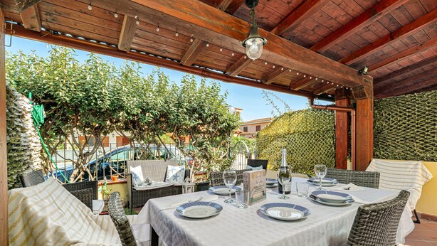 An outdoor patio with a table set for dining, wicker chairs, and a pergola overhead. - Holiday Home 'Villetta Via Tempio' with Private Terrace, Private Garden and Air Conditioning (San Teodoro)