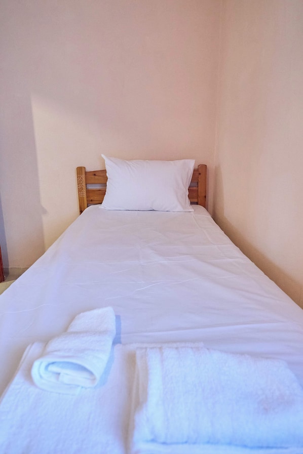 A single bed with white bedding and pillows, a wooden headboard, and a neatly folded towel on the bed.
