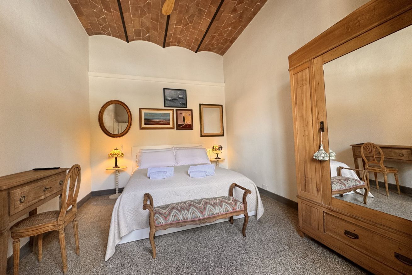 A bedroom with a large bed, a wooden dresser, a chair, a bench, and a mirror.