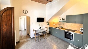 Eine kleine Küche mit Holzbalkendecke, einem Esstisch mit Stühlen, einem an der Wand befestigten Fernseher und einem Spülbecken.