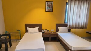 A hotel room with two single beds, a nightstand with a lamp, a small table, and a chair. - Abhushan Mahal (Degana)