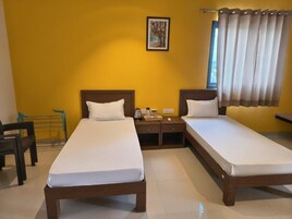 Una habitación de hotel con dos camas individuales, una mesita de noche con lámpara, una pequeña mesa y una silla.