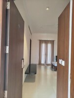 Habitación de hotel con puerta de madera, una mesita, un banco y una ventana con cortinas.