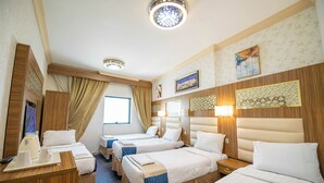 A hotel room with four beds, a desk, a window, and decorative wall panels. - Al Olayan Golden Hotel Misfalah (Makkah)