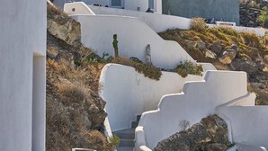 A white, curved building with multiple windows and a door, set against a hilly landscape. - Superior Windmill with a private jacuzzi (FC2M+X3 Imerovigli, Greece)
