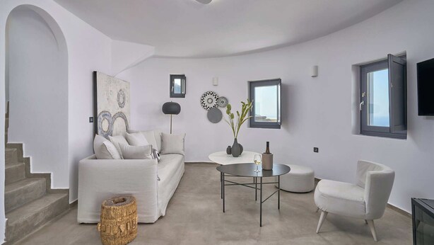A modern living room with a white sofa, a round coffee table, and a white armchair. There is a staircase on the left and a window on the right. - Superior Windmill with a private jacuzzi (FC2M+X3 Imerovigli, Greece)