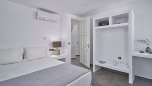 A modern bedroom with a bed, bedside lamp, air conditioning unit, and a walk-in closet with shelves and folded towels. - Superior Windmill with a private jacuzzi (FC2M+X3 Imerovigli, Greece)