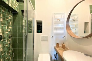 A bathroom with a glass shower enclosure, a white sink, a wooden vanity, and a mirror with a wooden frame. - CAMPOREGIO 31 - in the center with a view of the Duomo (Siena)