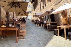 An outdoor café with wooden tables and chairs, covered by large umbrellas, set against a backdrop of brick buildings. - CAMPOREGIO 31 - in the center with a view of the Duomo (Siena)
