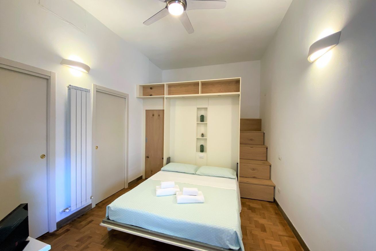 A bedroom with a bed, a ceiling fan, a radiator, a wardrobe, and a staircase.