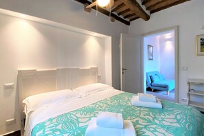 A bedroom with a bed, white headboard, and a green patterned bedspread. There are towels on the bed and a door leading to another room. - CAMPOREGIO 31 - in the center with a view of the Duomo (Siena)