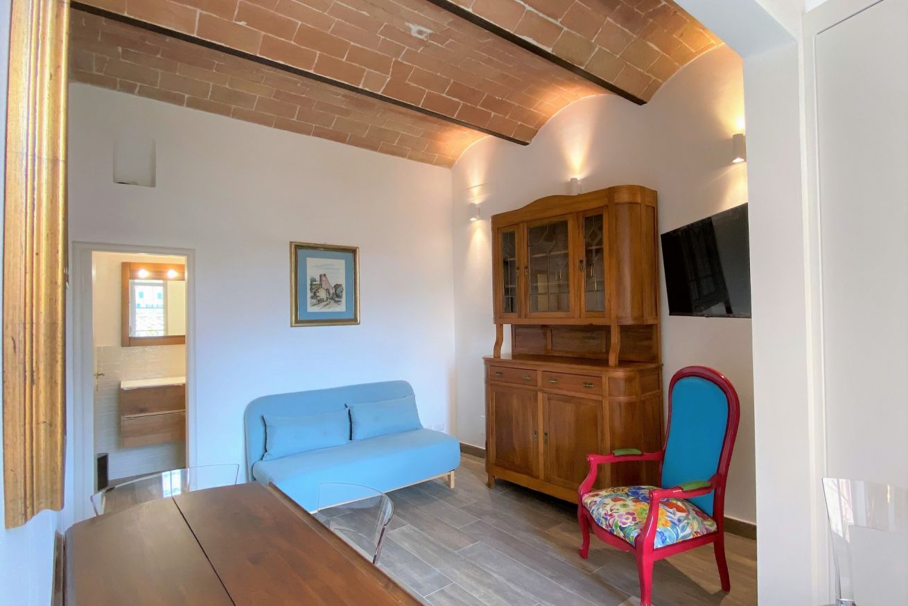A room with a blue sofa, a wooden cabinet, a red chair, and a TV mounted on the wall.