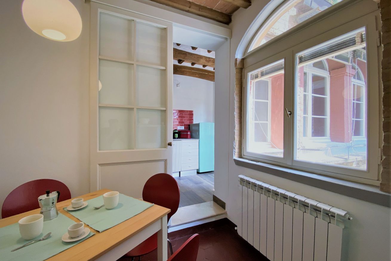 A dining area with a wooden table, red chairs, and a view of a kitchen through an open door.