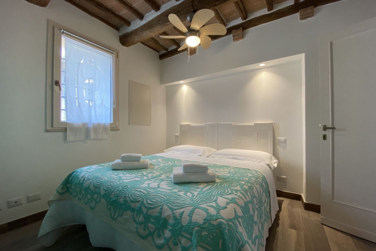 A bedroom with a bed, a ceiling fan, a window with blinds, and a door.